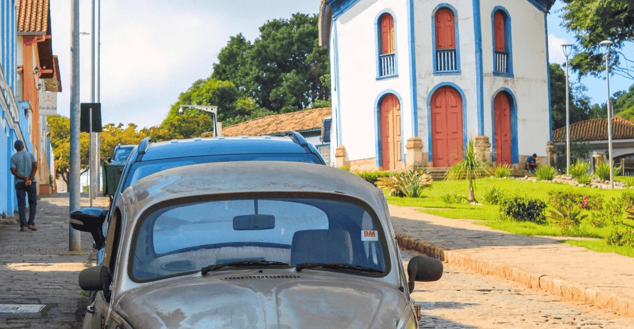 Fusca antigo em rua de pedra de Santa Bárbara MG com igreja histórica e jardim ao fundo