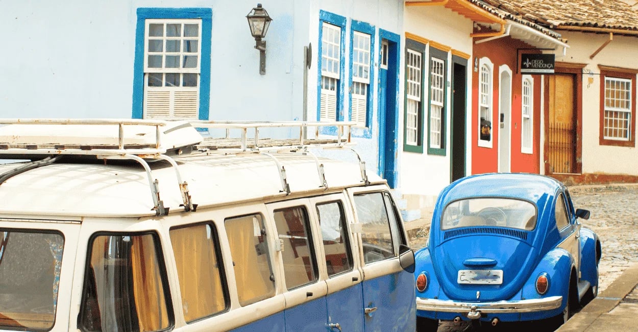 Fusca e kombi de cor azul, com casas coloridas do periodo colonial em São João del Rei