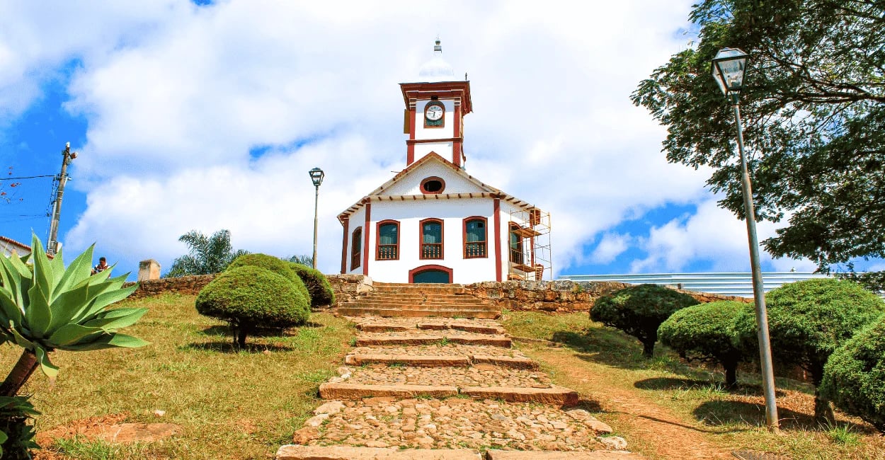 Igreja de Santa Rita em Serro MG vista pela escadaria de pedra com jardim e céu azul ao fundo