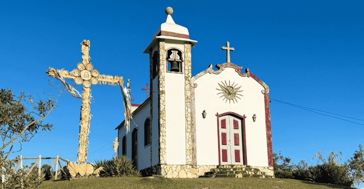 Igreja no Morro Redondo em Ipoema MG com cruzeiro ornamentado, torre com sino e céu azul