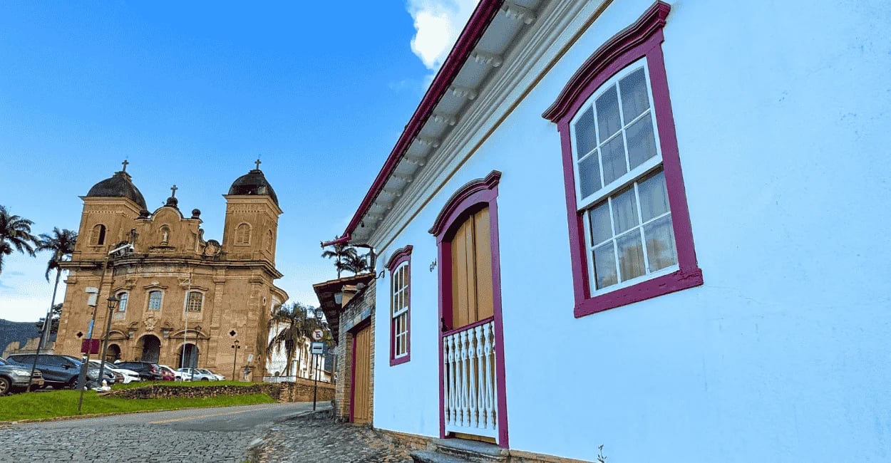 Centro histórico de Mariana MG com casario colonial branco, janelas coloridas, rua de pedra e igreja