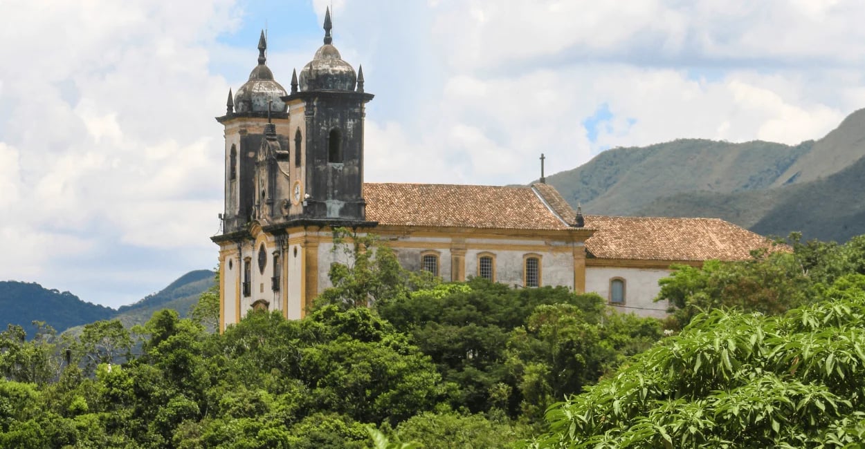 Igreja histórica em Ouro Preto cercada por vegetação, montanhas e paisagem colonial mineira ao fundo