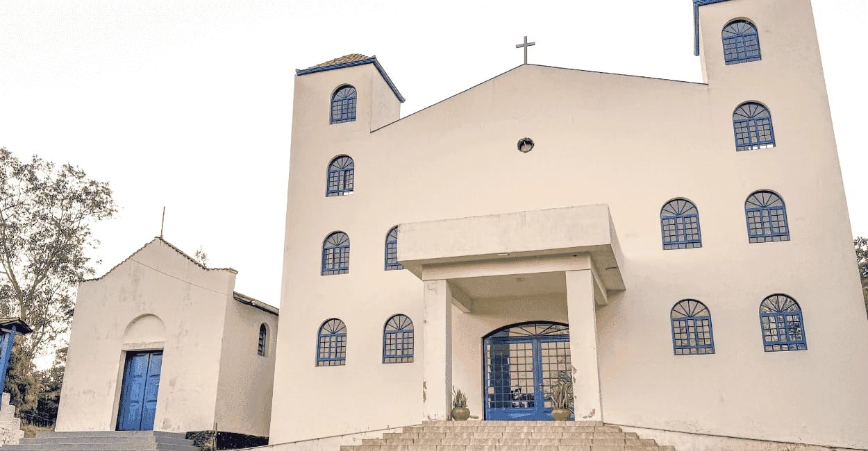 Igreja de cor branca e janelas azuis, com escada branca e céu nublaco em Casa Branca