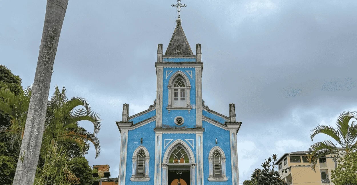 Igreja de Lagoa Dourada com cores azuis, céu nublado e coqueiros em volta