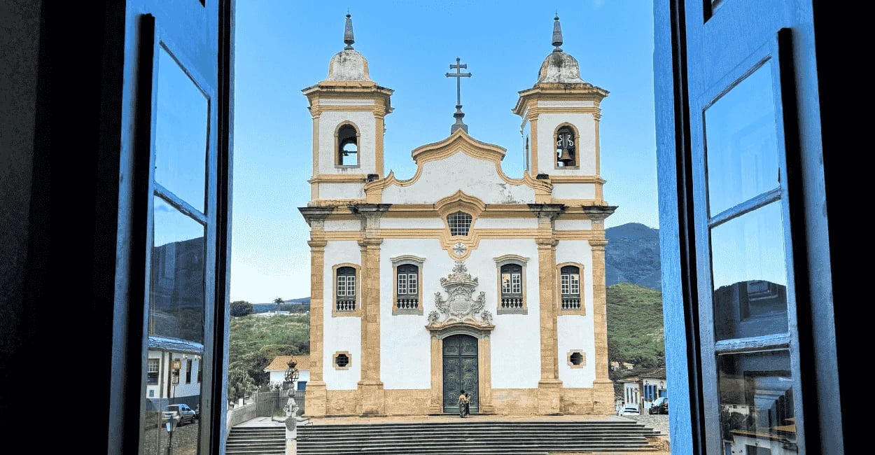 Igreja histórica de Mariana MG vista pela janela azul, com montanhas ao fundo em destaque