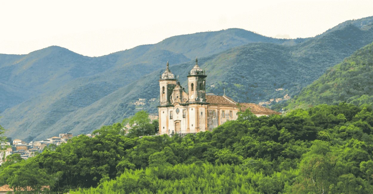 Igreja histórica destacada no alto da colina e cercada por muito verde em Ouro Preto, MG