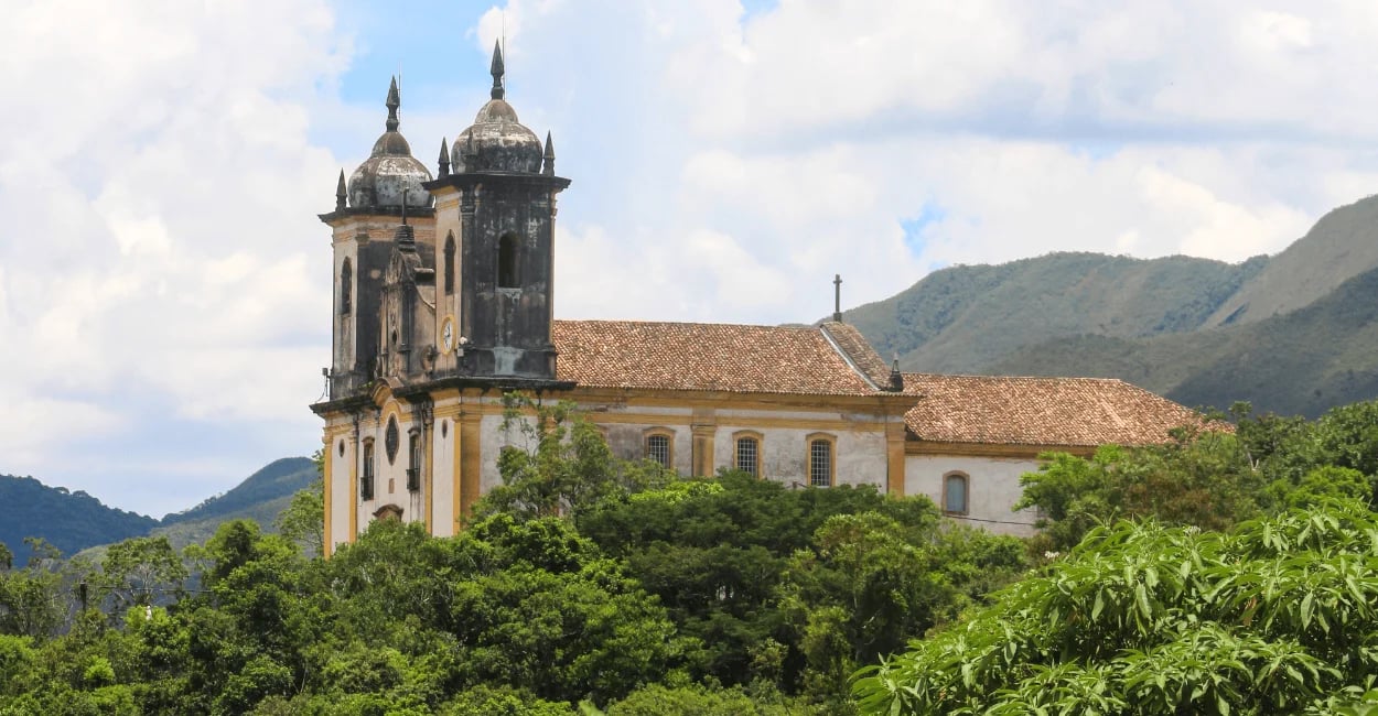 Igreja histórica em Ouro Preto MG cercada por vegetação verde e montanhas ao fundo