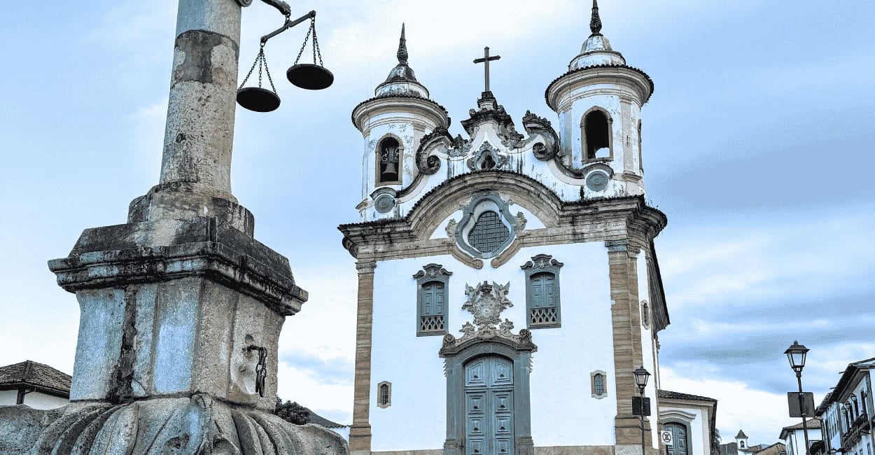 Igreja histórica de Mariana com torres barrocas, pelourinho em destaque e céu nublado ao fundo