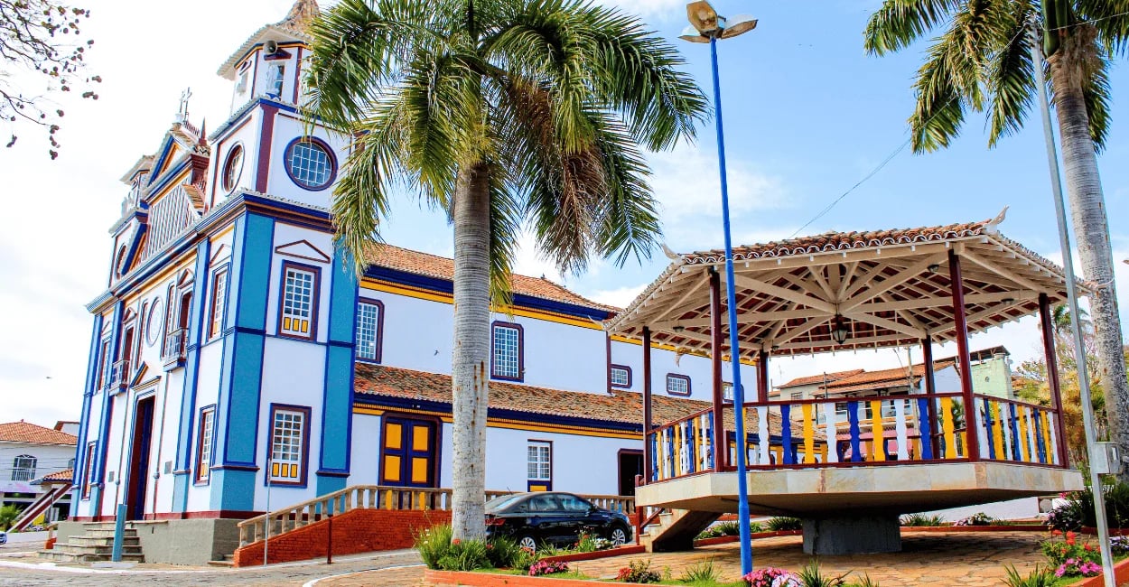 Igreja Matriz e coreto na praça de Datas MG com arquitetura colonial, palmeiras e praça com cores
