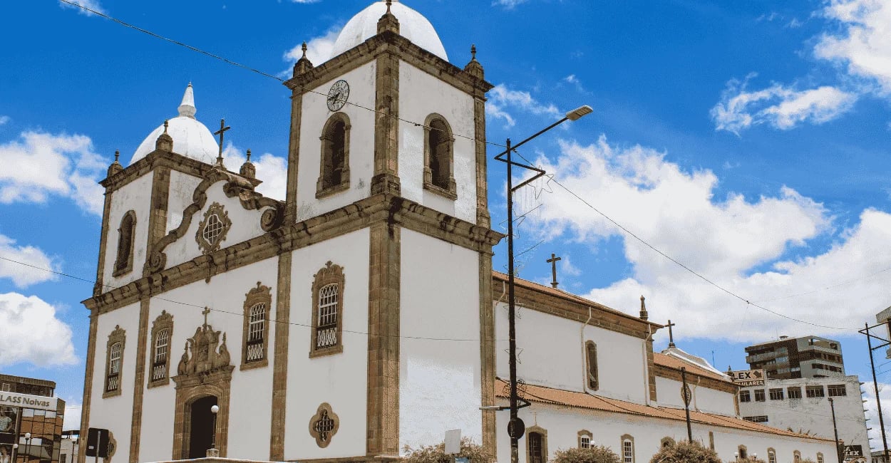 Igreja histórica de Barbacena com torres brancas, detalhes em pedra e céu azul ao fundo