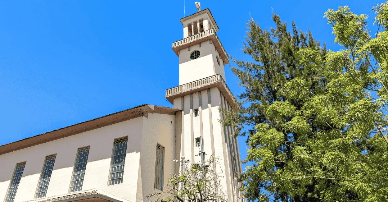Torre alta e fachada clara da imponente Igreja Matriz de Carandaí cercada por folhagens verdes