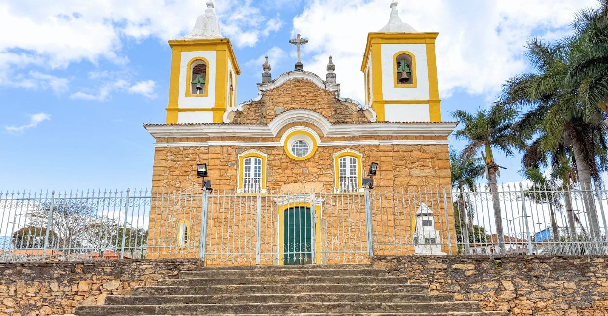 Fachada da Igreja Matriz de Carrancas, em Minas Gerais, com torres amarelas, paredes de pedra
