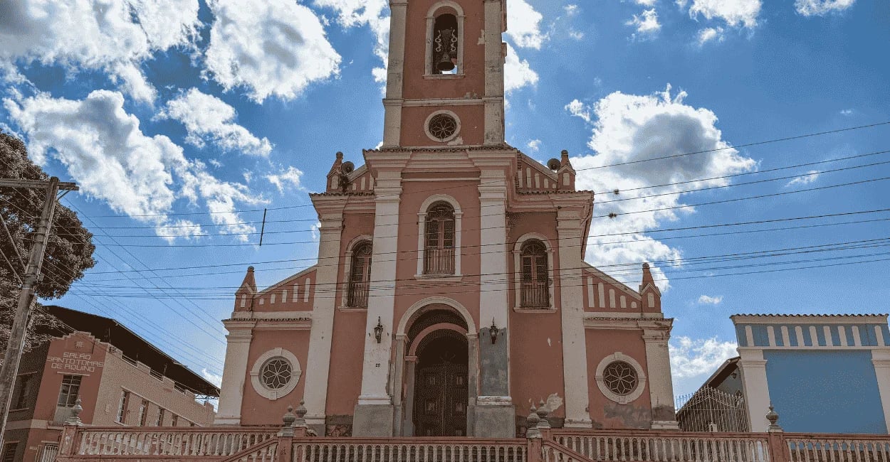 Igreja Matriz de fachada rosa e branca sob céu azul em Dores de Campos, Minas Gerais