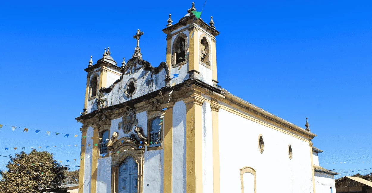 Igreja Matriz de Itatiaia MG com fachada colonial branca e amarela sob céu azul intenso