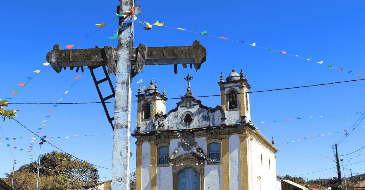 Cruzeiro em primeiro plano diante de igreja histórica em Itatiaia distrito de Ouro Branco MG, sob cé
