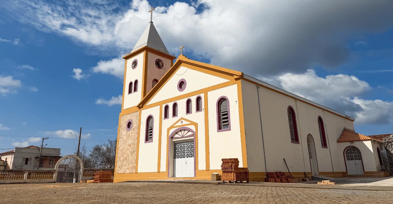 Igreja Matriz de Itutinga com torre lateral, fachada clara e detalhes amarelos sob céu azul