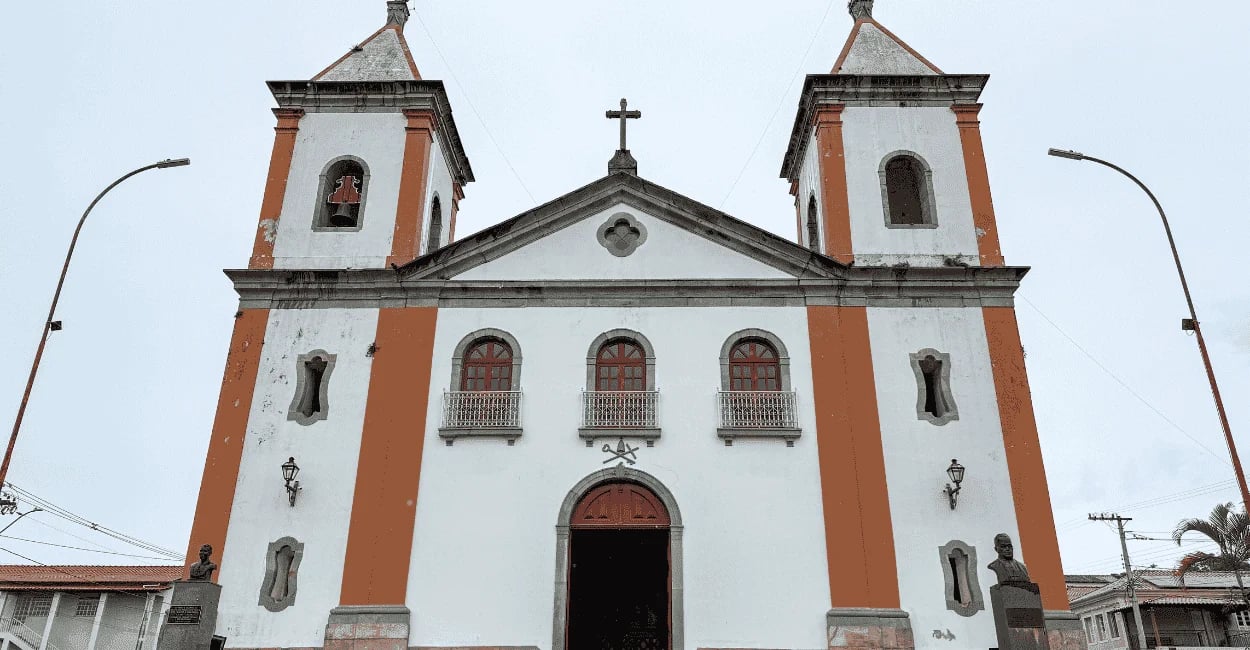 Igreja histórica branca com detalhes verticais laranjas e bustos na entrada em Lagoa Dourada