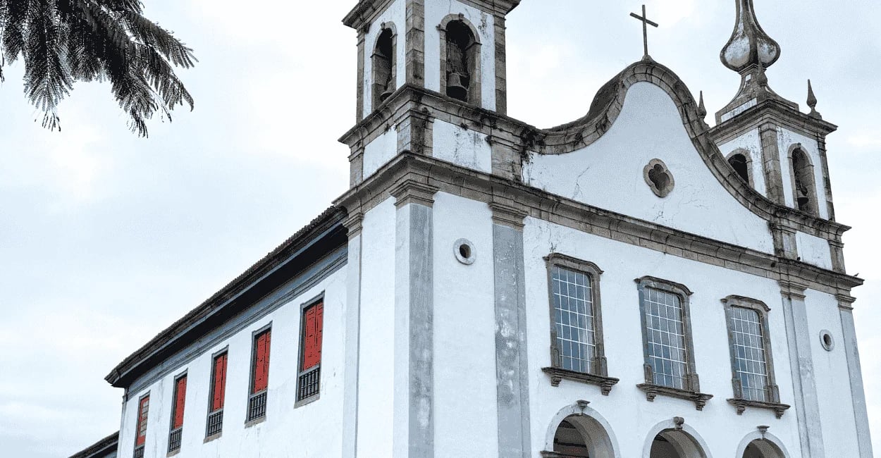 Igreja Matriz de Catas Altas MG com fachada colonial branca, janelas vermelhas e torres sineiras