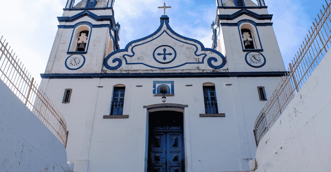Igreja Matriz de Raposos, em Minas Gerais, com fachada branca e detalhes azuis vista de baixo