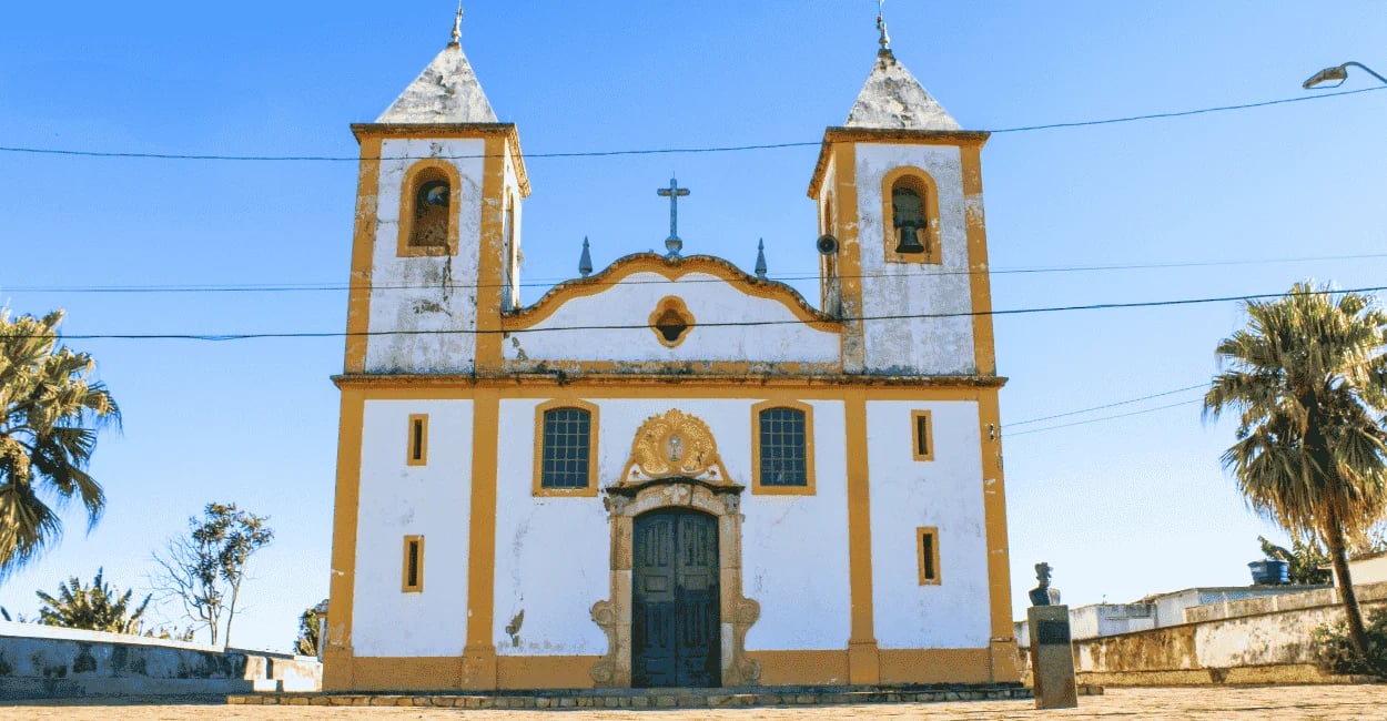 Igreja Matriz de Santo Amaro, com cor branca e amarela, céu sem nuvens em Queluzito MG