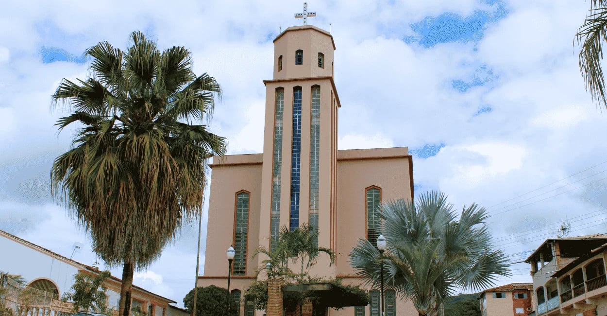 Igreja Matriz de Morro do Pilar sob céu nublado, emoldurada por palmeiras