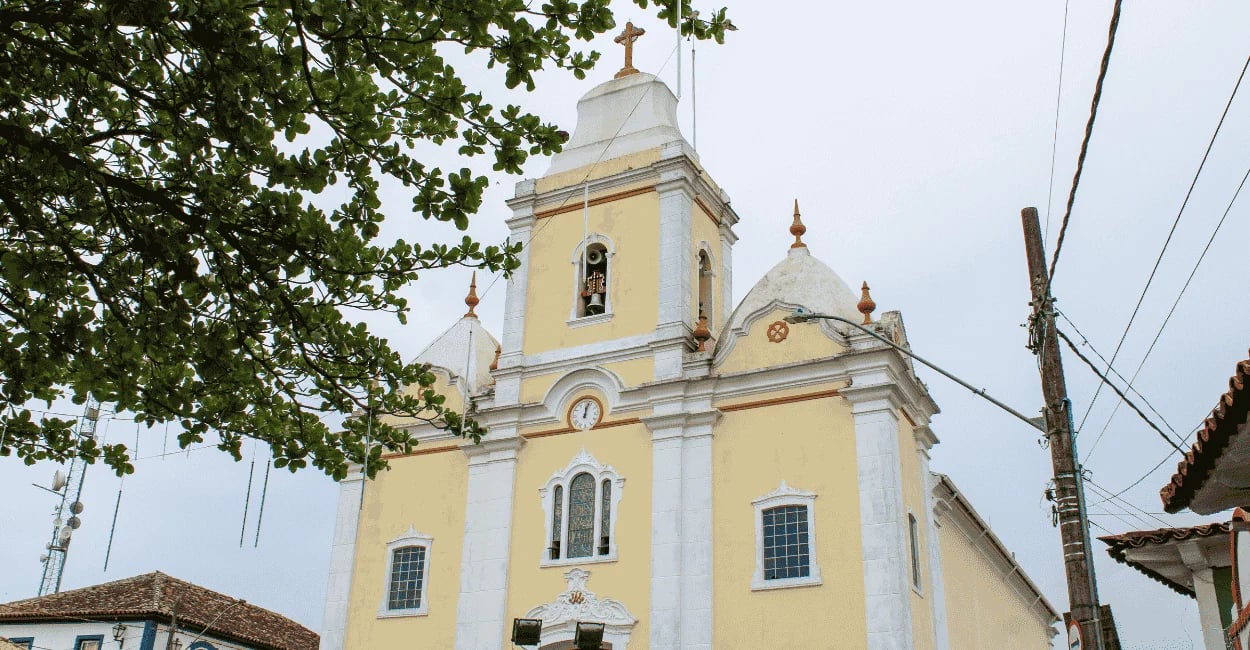 Igreja Matriz de Resende Costa em Minas Gerais, com fachada amarela e branca vista sob árvores