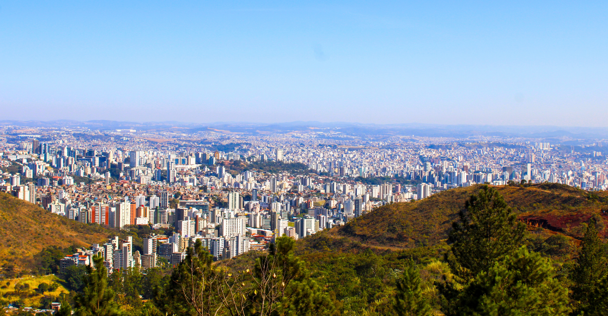 Vista de um mirante da cidade de Belo Horizonte, com prédios, casas, montanhas e um céu aberto