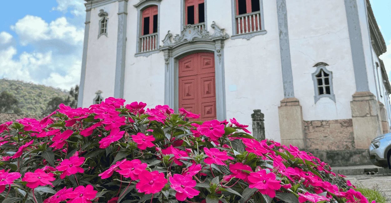 Flores rosas em frente à igreja histórica de Santa Bárbara, com fachada colonial ao fundo
