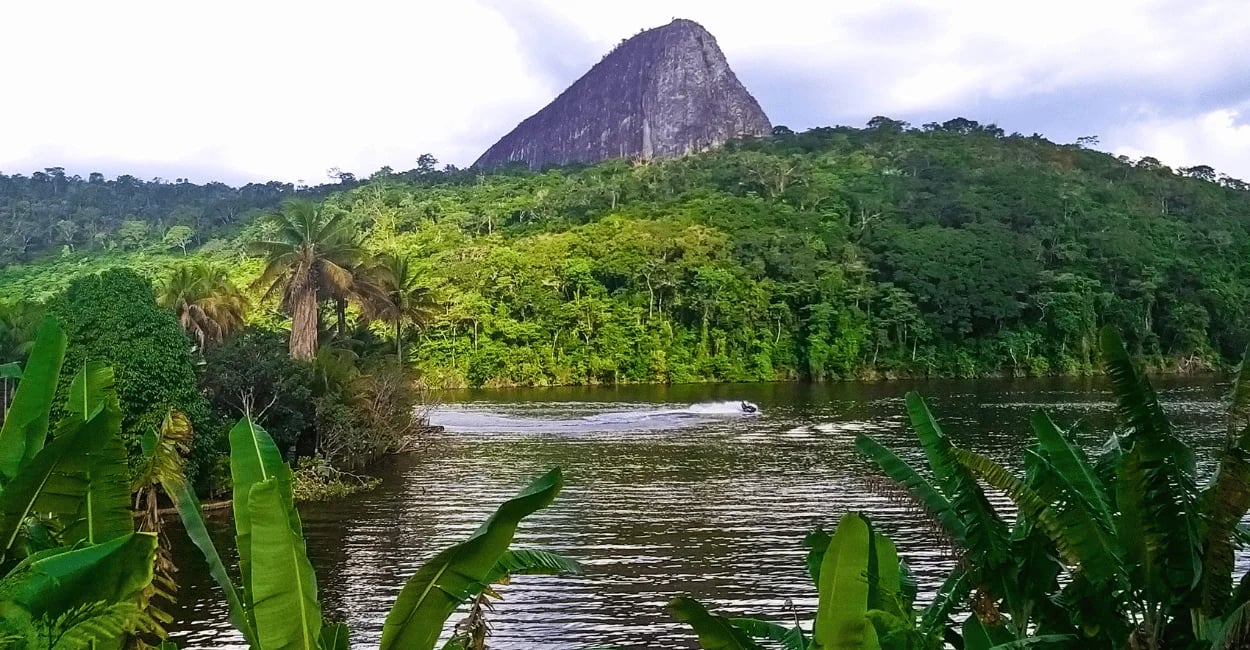 Lago cercado por vegetação com grande formação rochosa ao fundo em Ladainha, Minas Gerais