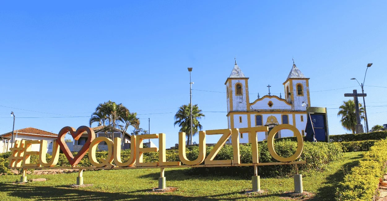 Letreiro Eu Amo Queluzito na praça central com igreja matriz ao fundo em Minas Gerais