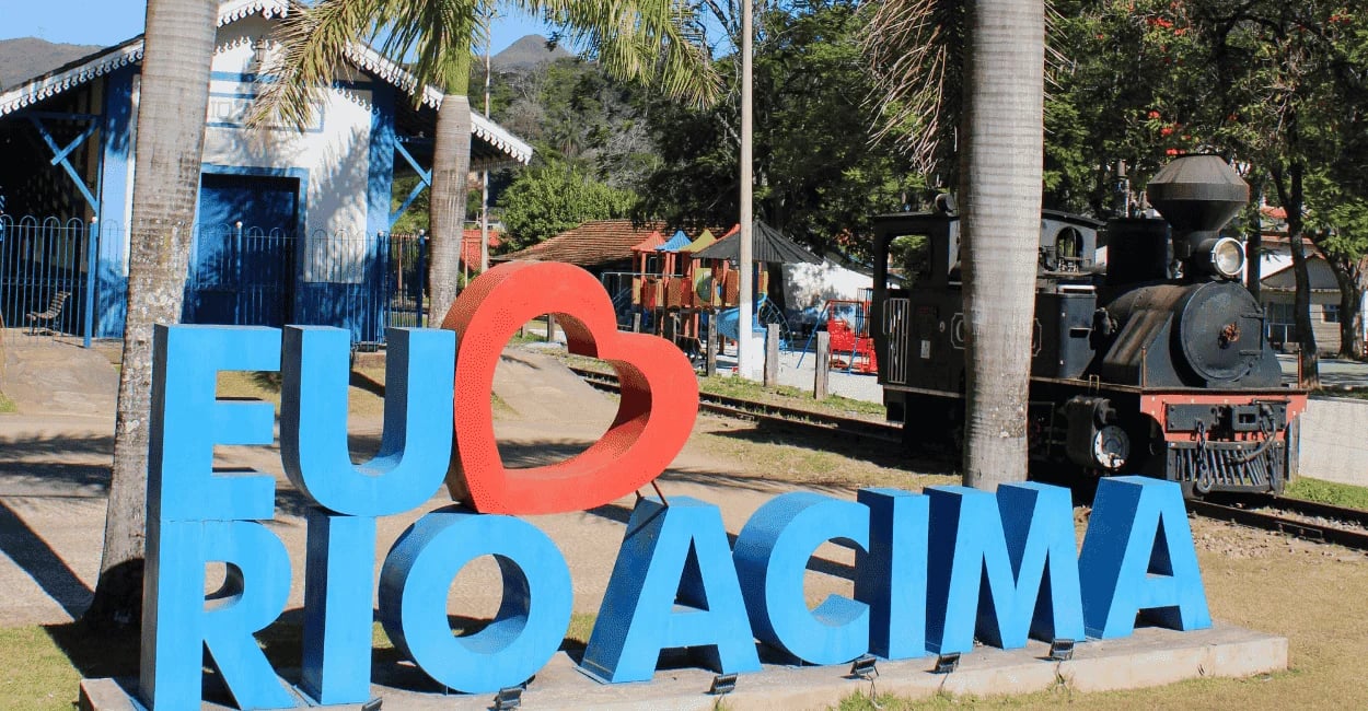 Letreiro Eu amo Rio Acima com locomotiva histórica, estação ferroviária e palmeiras, área turística