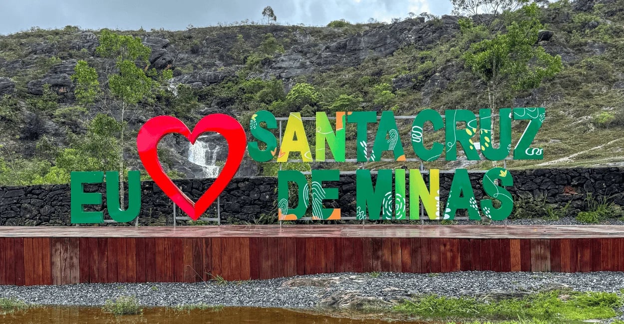Letreiro de Santa Cruz de Minas com coração vermelho diante da serra de são josé e cachoeira