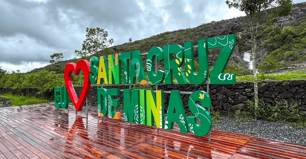 Letreiro turístico de Santa Cruz de Minas MG em deck molhado com cachoeira e paredão rochoso
