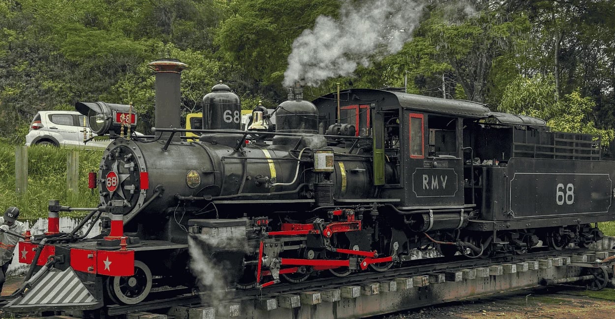 Locomotiva a vapor Maria Fumaça preta puxando vagões verdes na estação colonial de Tiradentes, MG