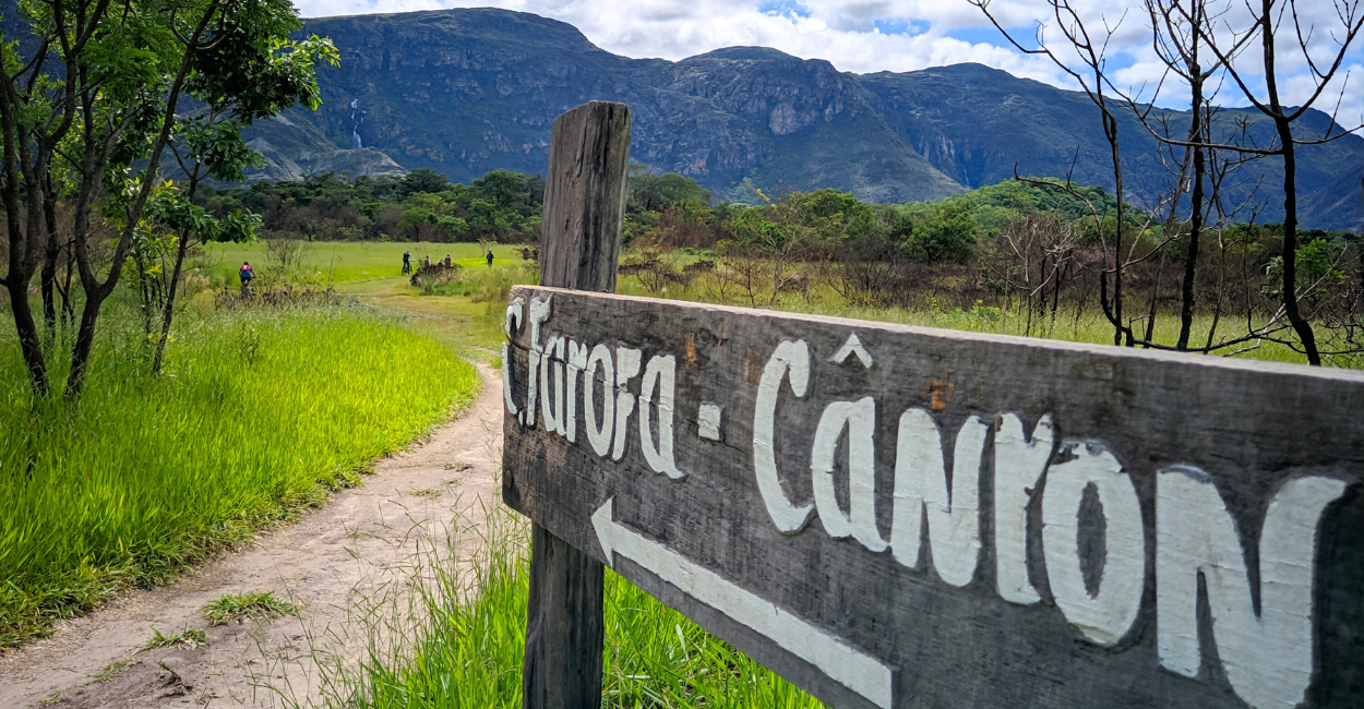 Placa de indicação da cachoeira da Farofa, com cachoeira, vegetação e montanhas ao fundo