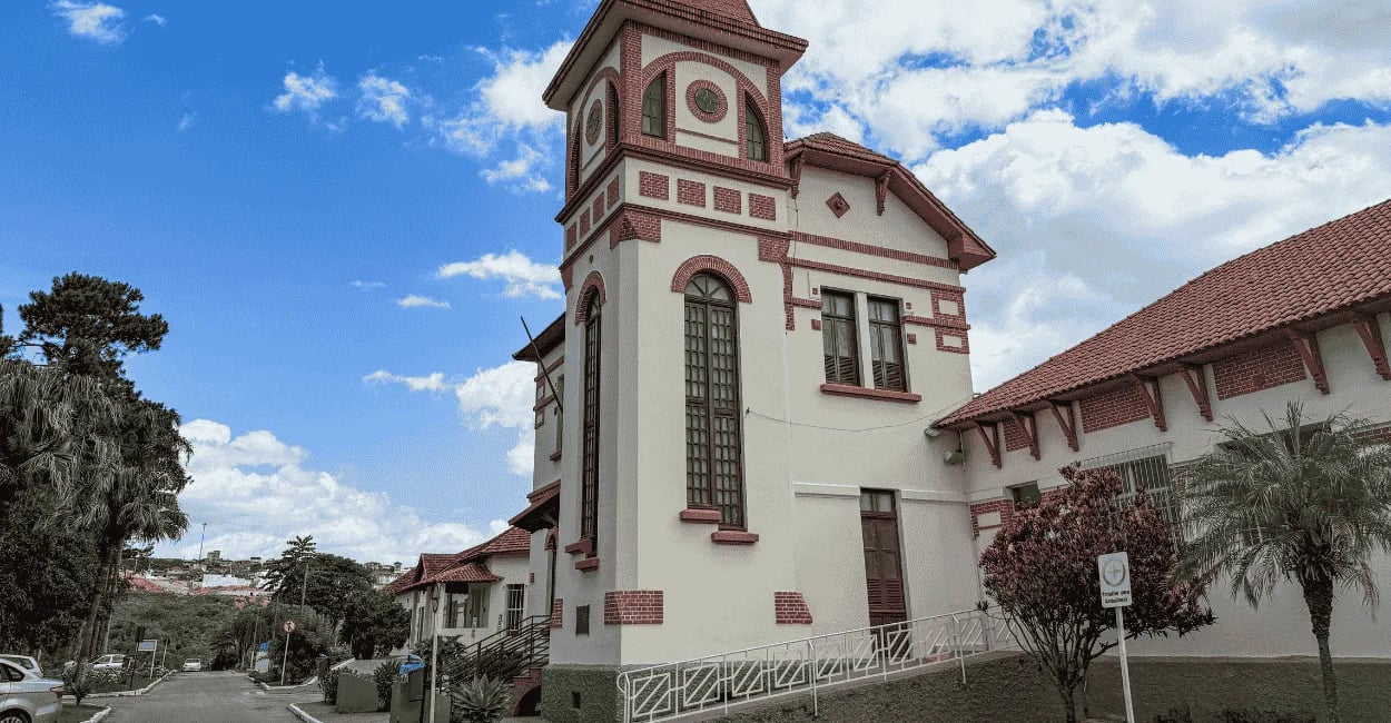 Museu da loucura em Barbacena, prédio de cor branca e detalhes em cor rosa, céu azul com nuvens