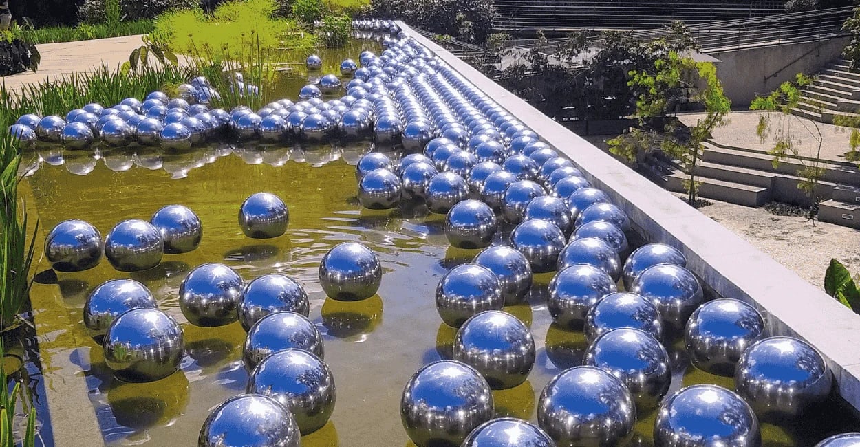 Jardim de Narciso no Inhotim com esferas espelhadas sobre a água e reflexos do céu azul