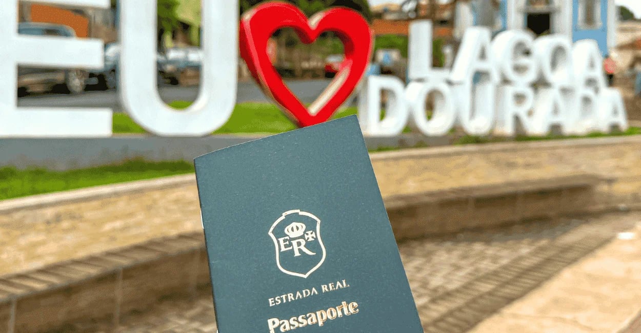 Capa verde do Passaporte da Estrada Real em frente ao letreiro Eu Amo Lagoa Dourada