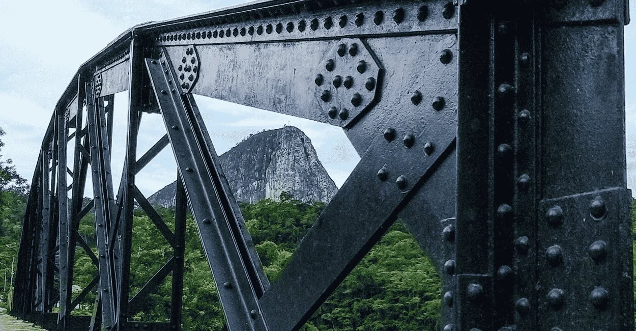 Pontilhão de Ferro, com a Pedra que é ponto turistico da cidade ao fundo e árvores, em Ladainha MG