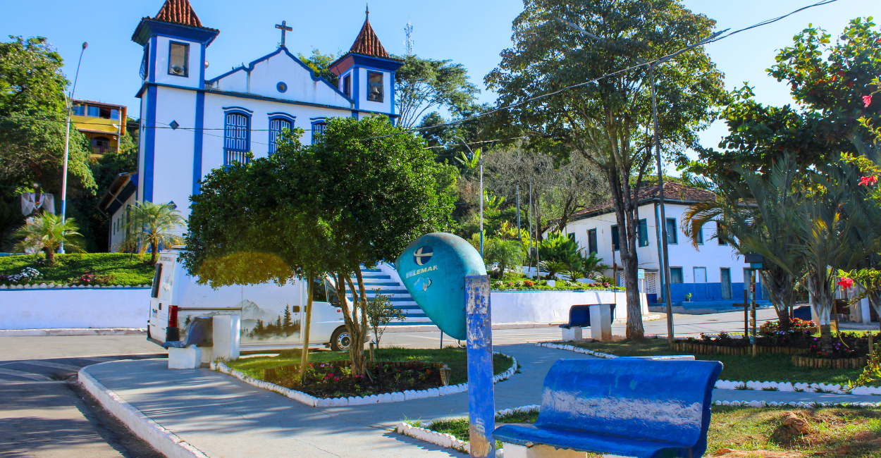 Praça central de Ipoema, com um banco, orelhão e a igreja matriz no fundo. Destino turistico em MG