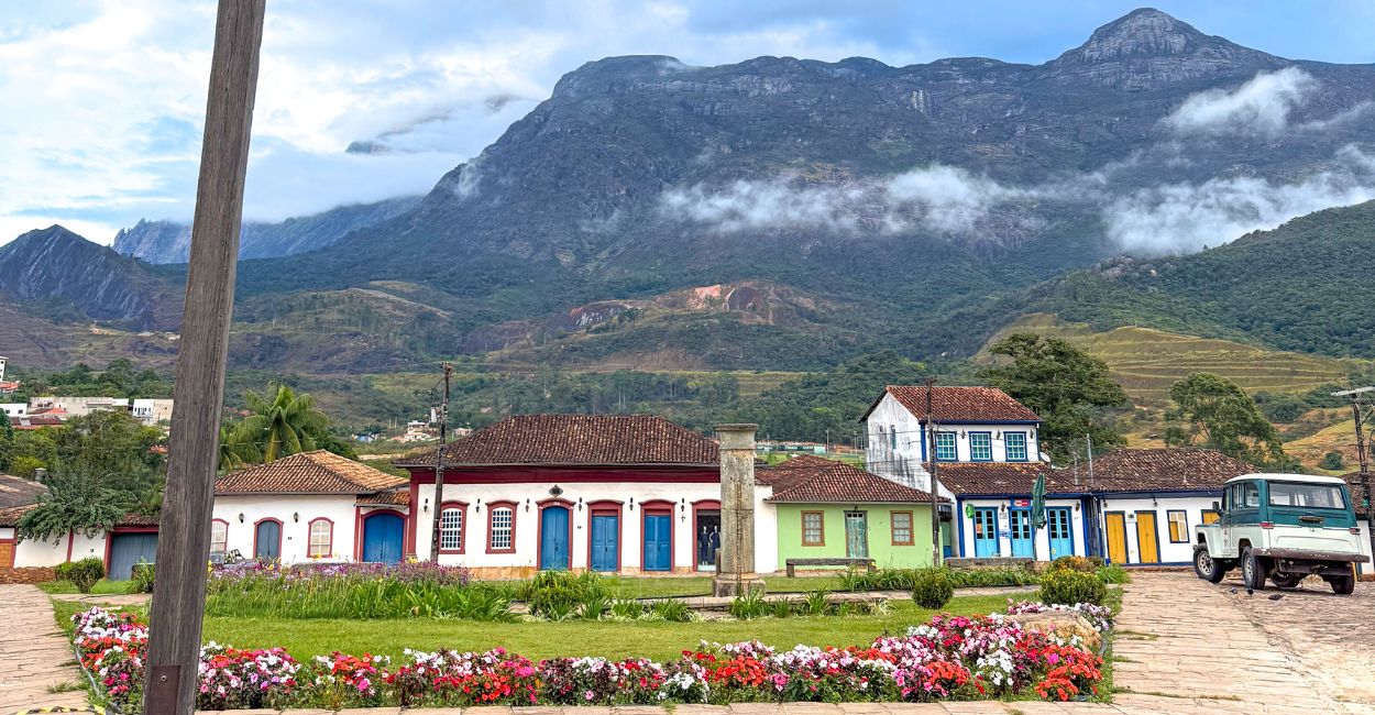 Praça central com rosas, ao fundo montanhas e casas históricas em Catas Altas MG