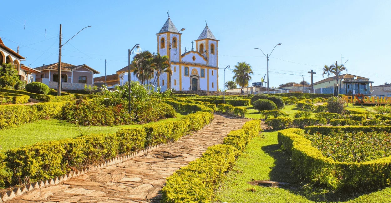 aminho de pedra em praça arborizada com a Igreja Matriz ao fundo. Queluzito, MG