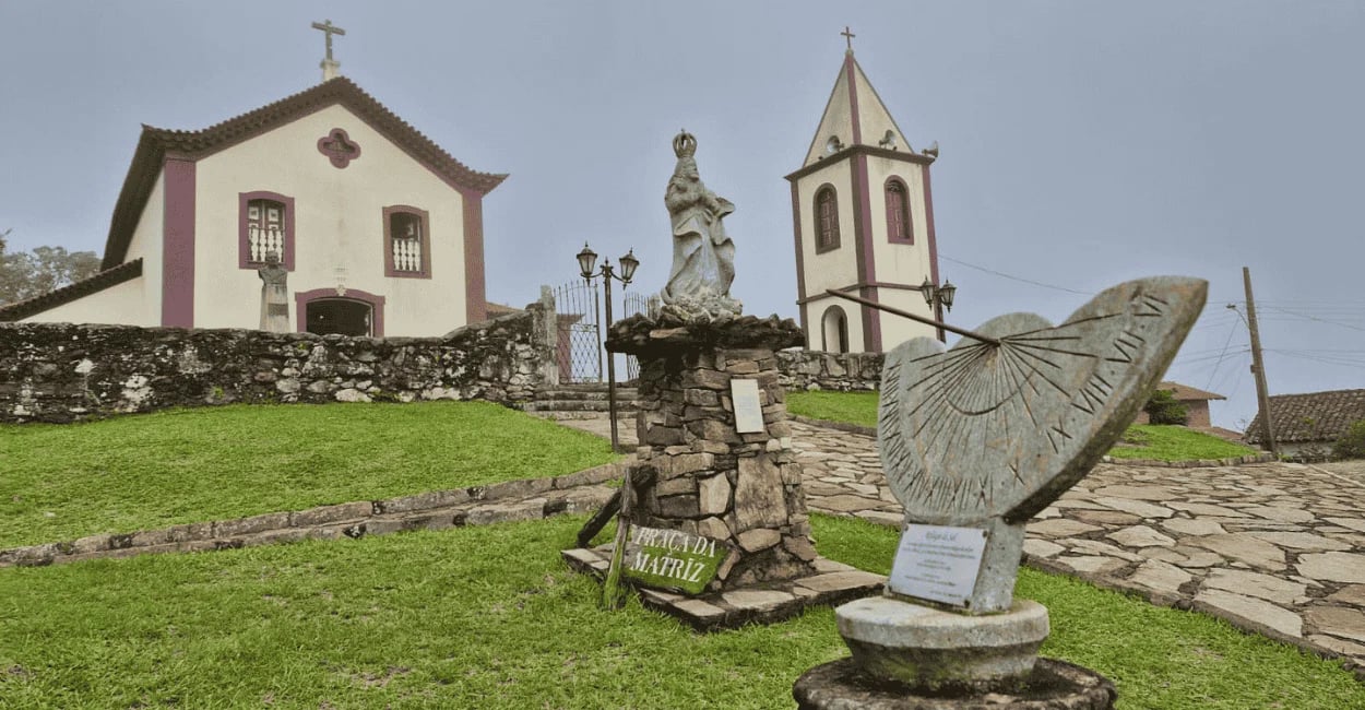 Igreja de Ibitipoca em área elevada, com fachada clara, torre, gramado e monumentos de pedra