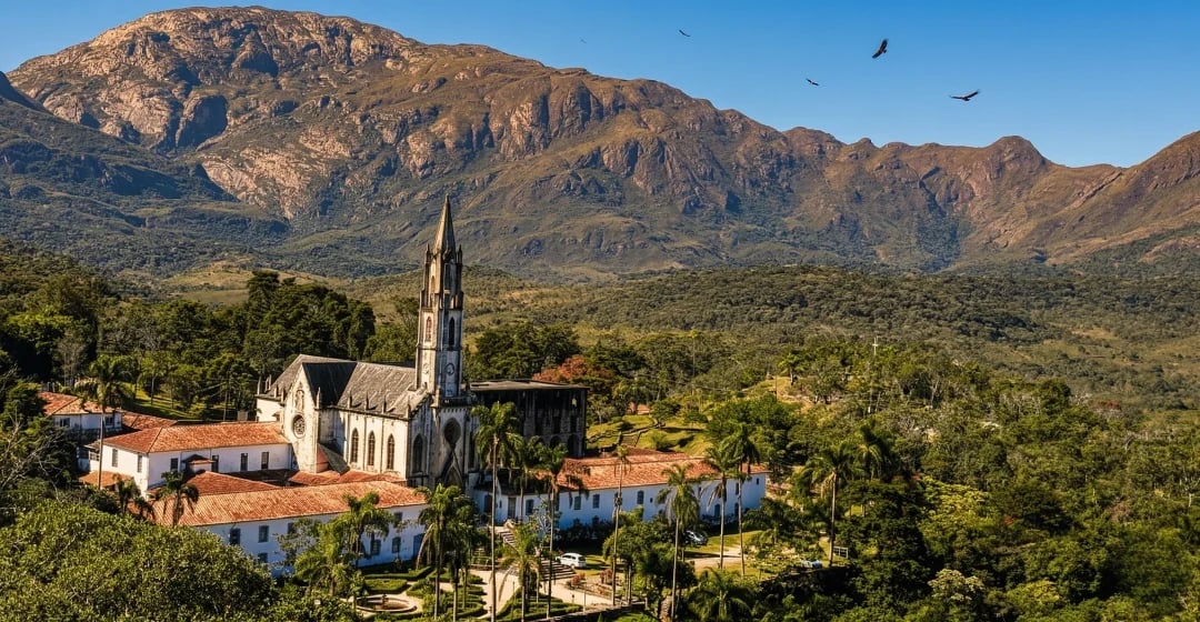 Santuário do Caraça em meio à natureza, com igreja histórica, palmeiras e a serra imponente ao fundo