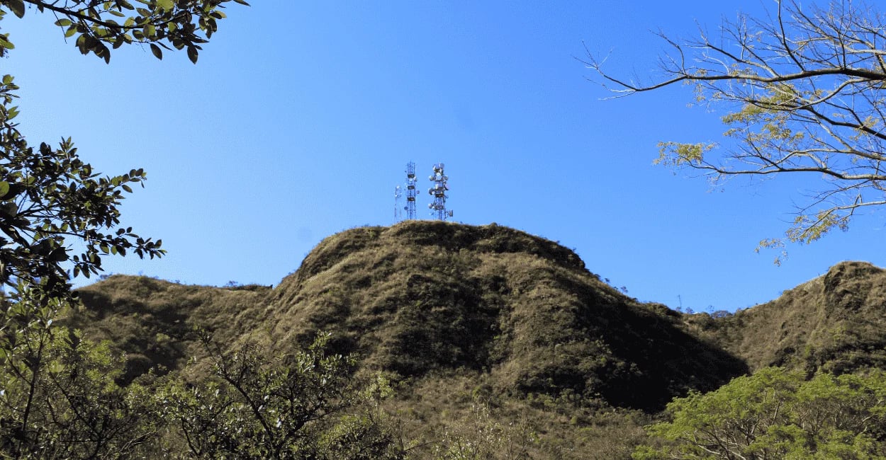 Pico da Serra do Curral em Belo Horizonte visto de baixo, com antenas, vegetação e céu azul