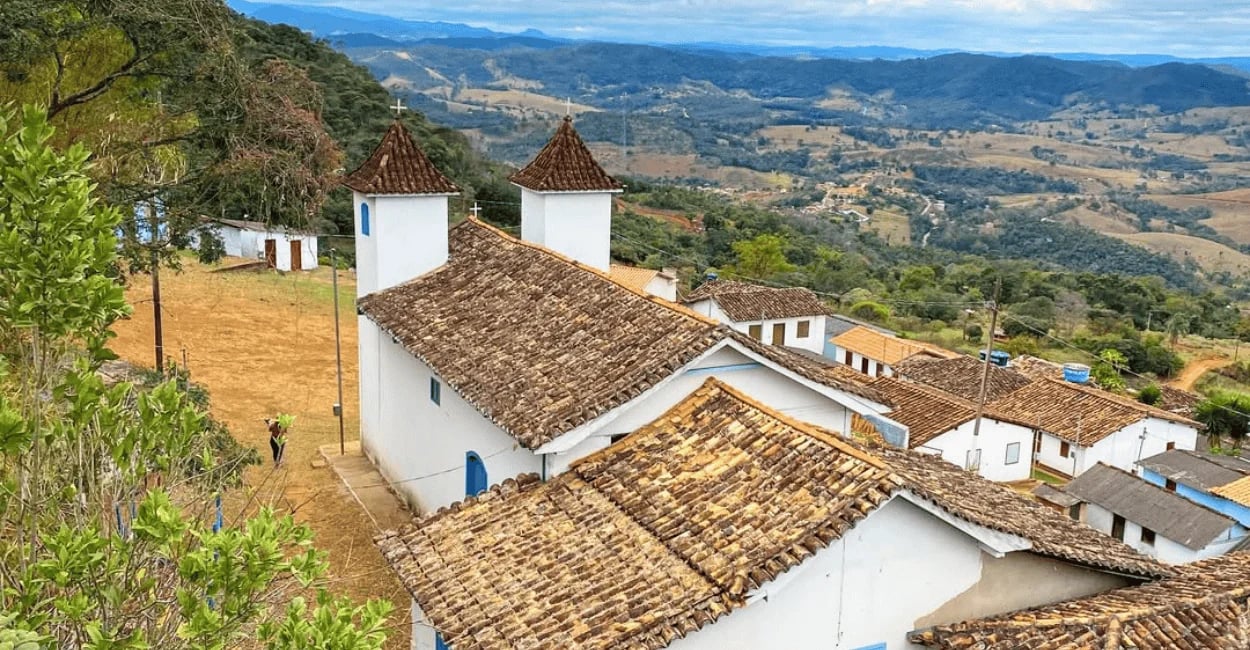 Vista panorâmica da igreja da Serra do Carola MG com telhados coloniais, casario simples e montanhas