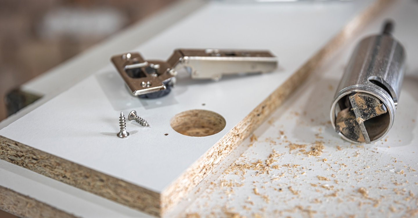 Montaż zawiasów puszkowych w płycie meblowej – nawiercony otwór, zawias i wkręty