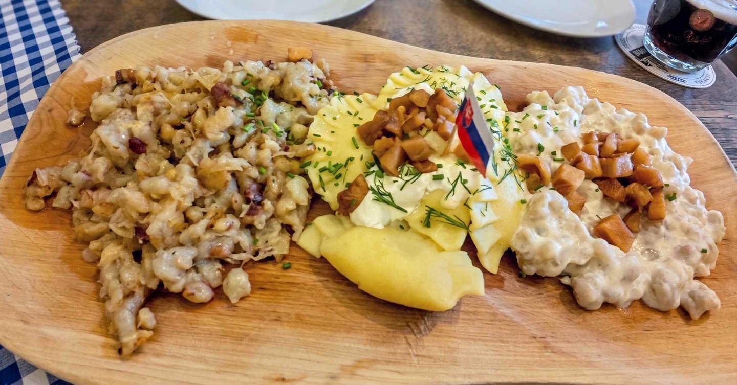 Plato combinado de comida tradicional eslovaca: bryndzové halušky y pírohy servidos en madera