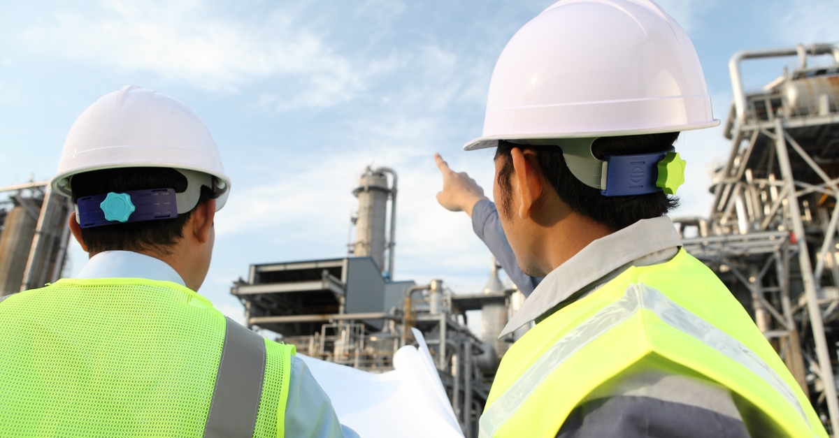 two men in safety vests standing in front of a factory