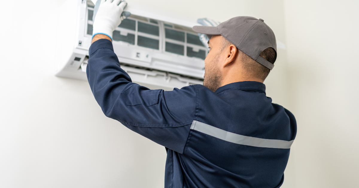 Un hombre con camisa azul y guantes blancos está arreglando un aire acondicionado.